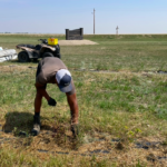 Summer student bent over pulling weeds in field