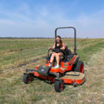 Summer student sitting on zero-turn mower, cutting grass in field