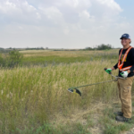 Summer student smiling for photo while holding wipper snipper on recreational trail