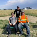 Three summer students posing for photo while sitting on bench on recreational trail