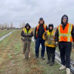 Four summer students covered in mud, posing for photo during tree planting in the rain